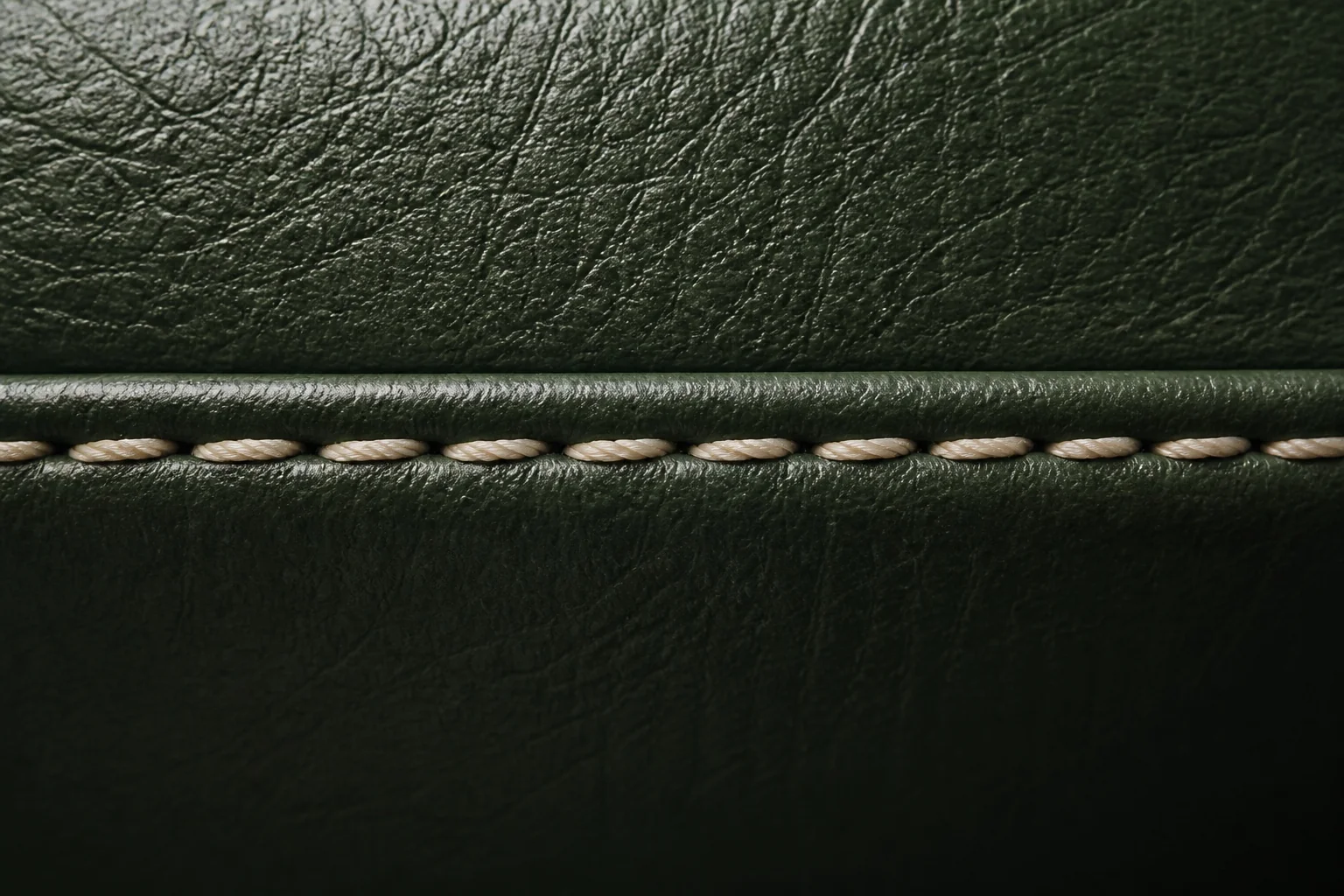 Close detail of cream stitching across deep green leather.